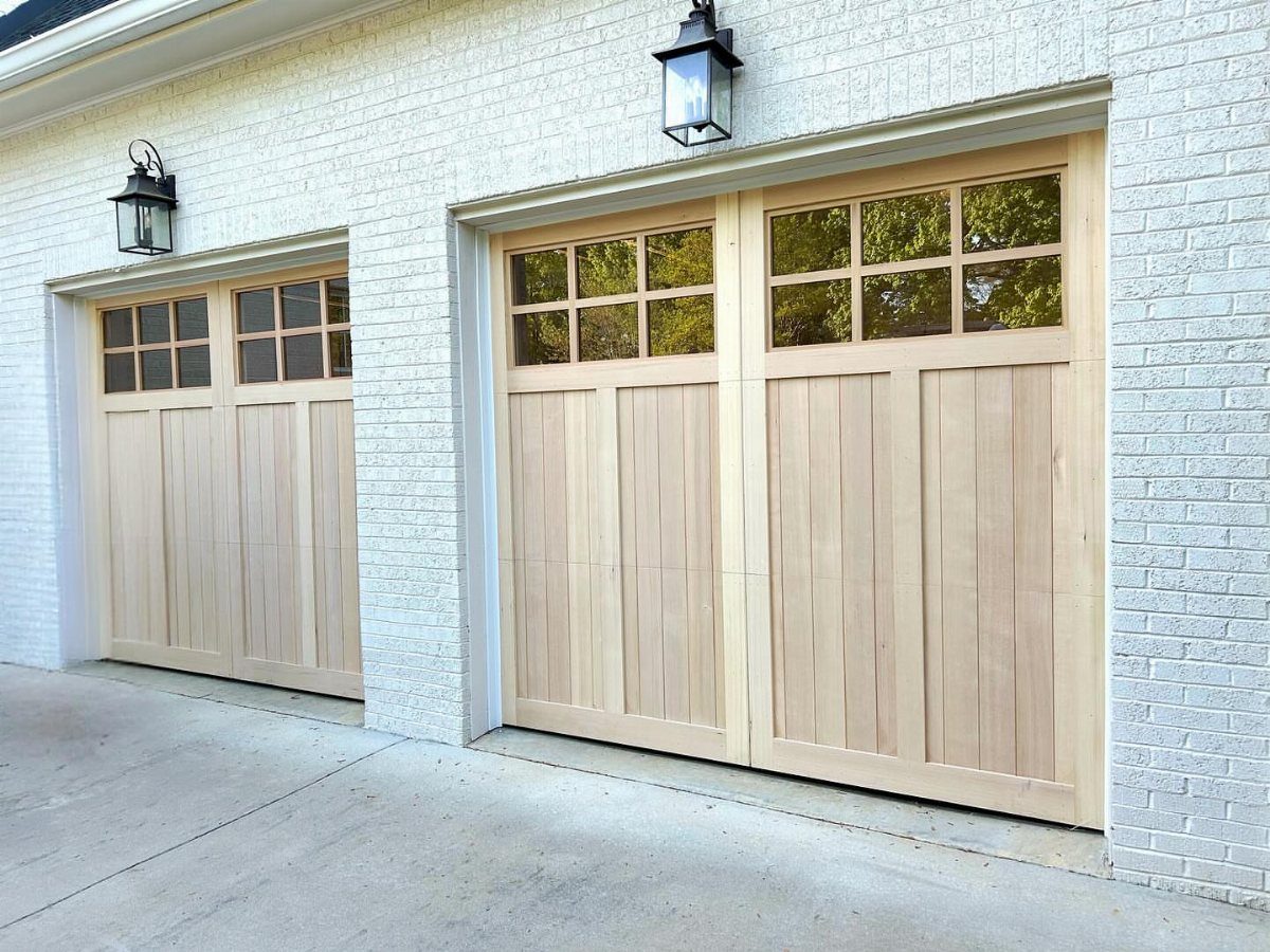 Two light wood craftsman style garage doors with window panes on a white brick house.