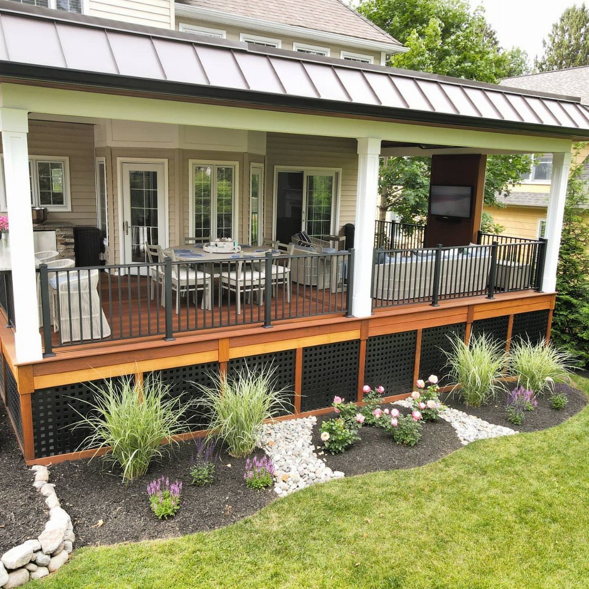 A covered wooden deck with a metal roof, outdoor furniture, and a landscaped garden area.