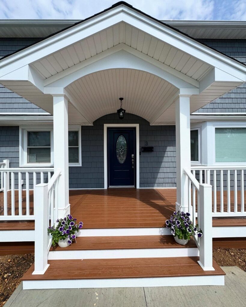 A brown wooden front deck with white railings and steps leading to a blue house door.