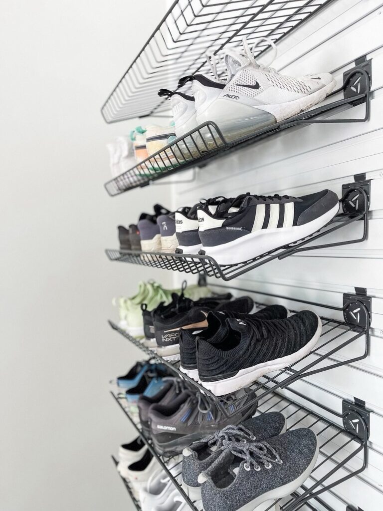 Black wire mesh shelves mounted on a white slatwall holding various pairs of athletic sneakers.