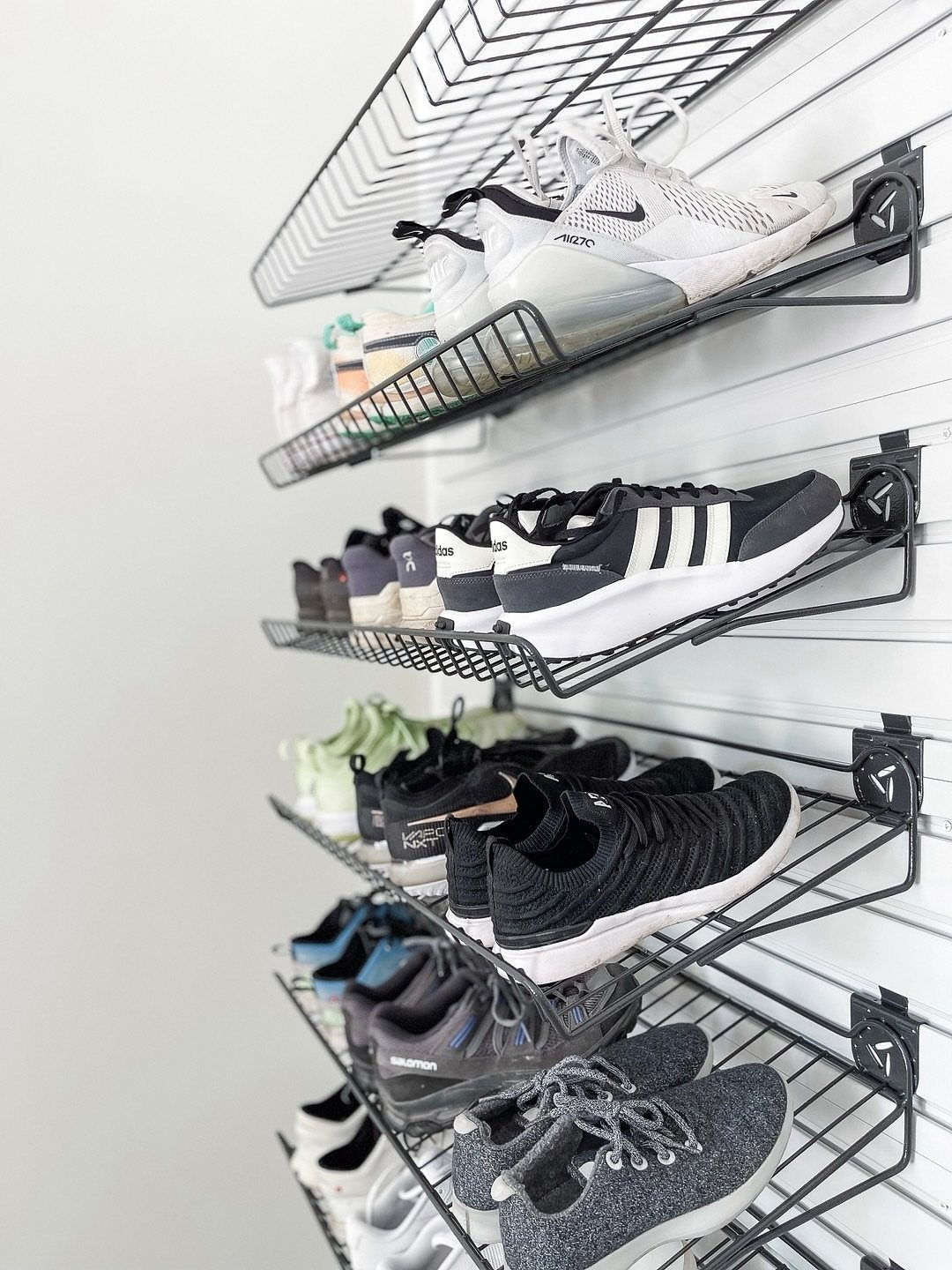 Black wire mesh shelves mounted on a white slatwall holding various pairs of athletic sneakers.