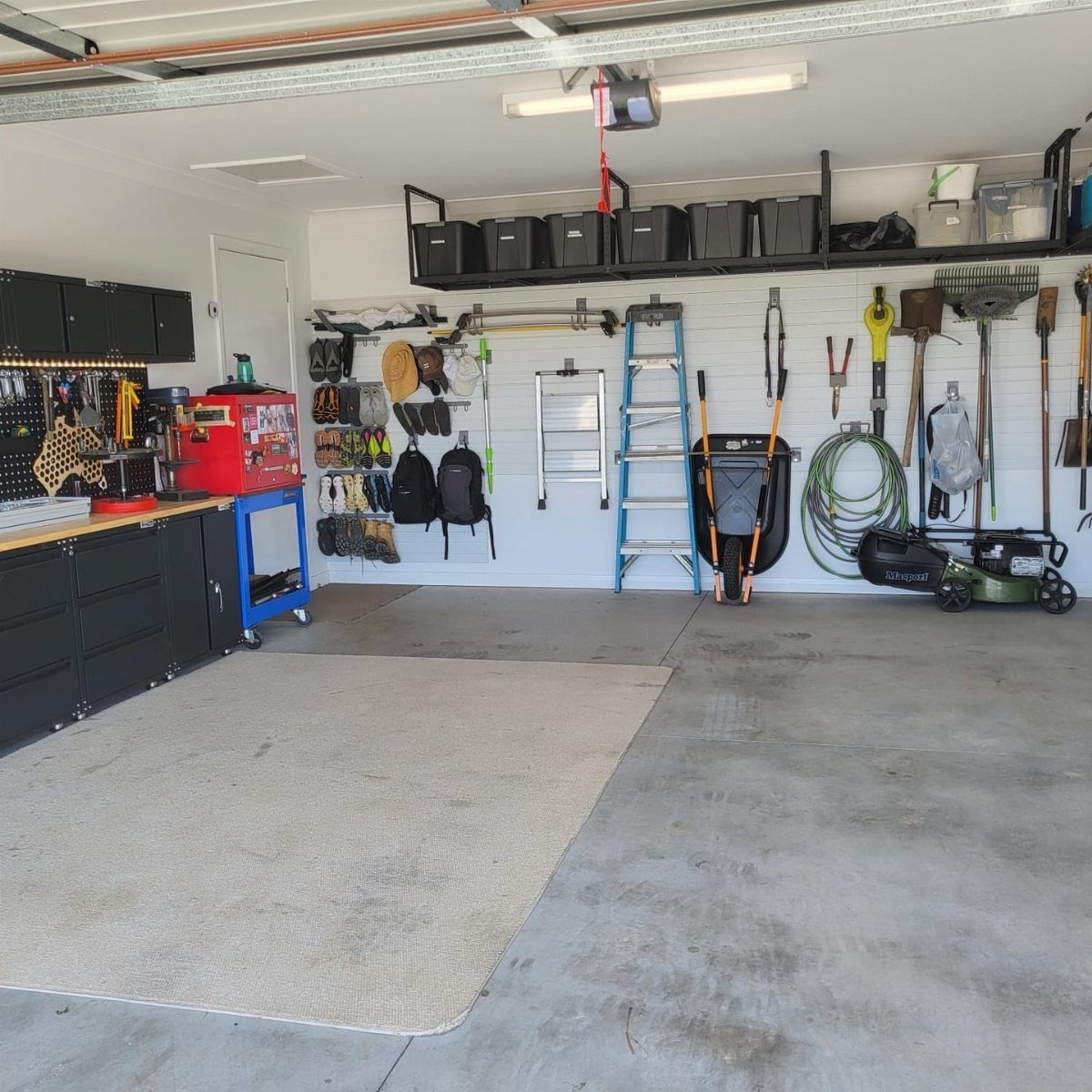 Organized garage featuring wall-mounted tools, black storage bins on high shelves, and a blue ladder.