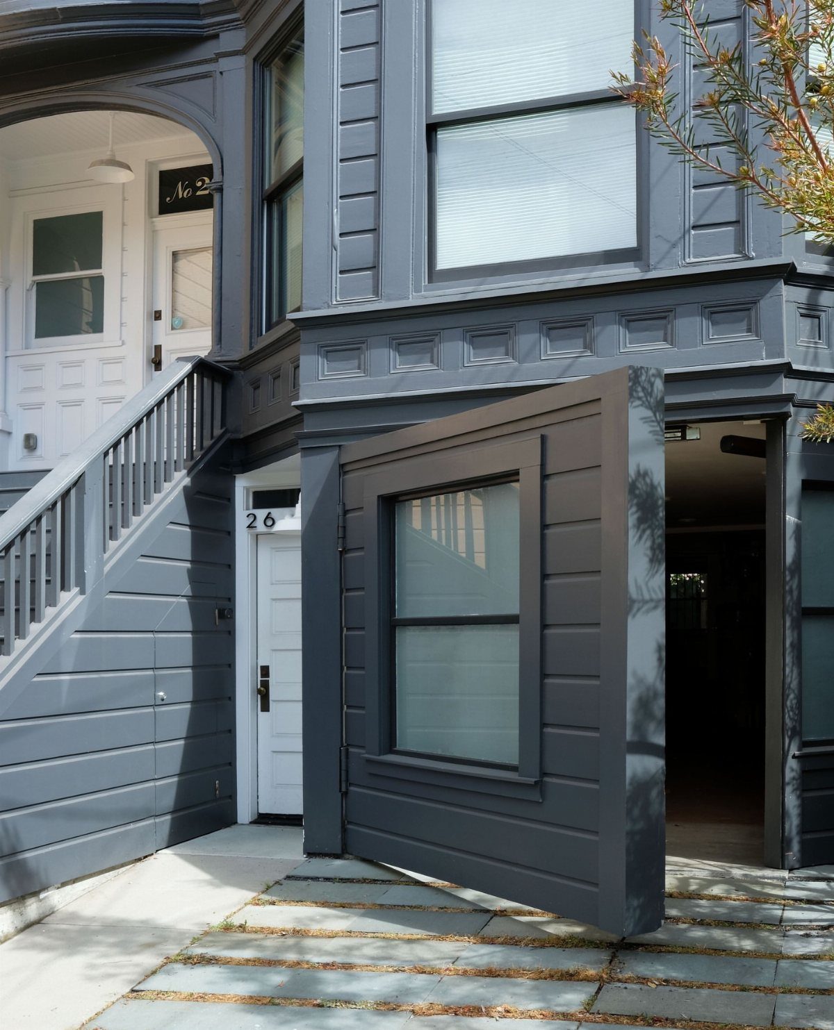 A large, dark grey pivoting garage door with a window on a modern house.