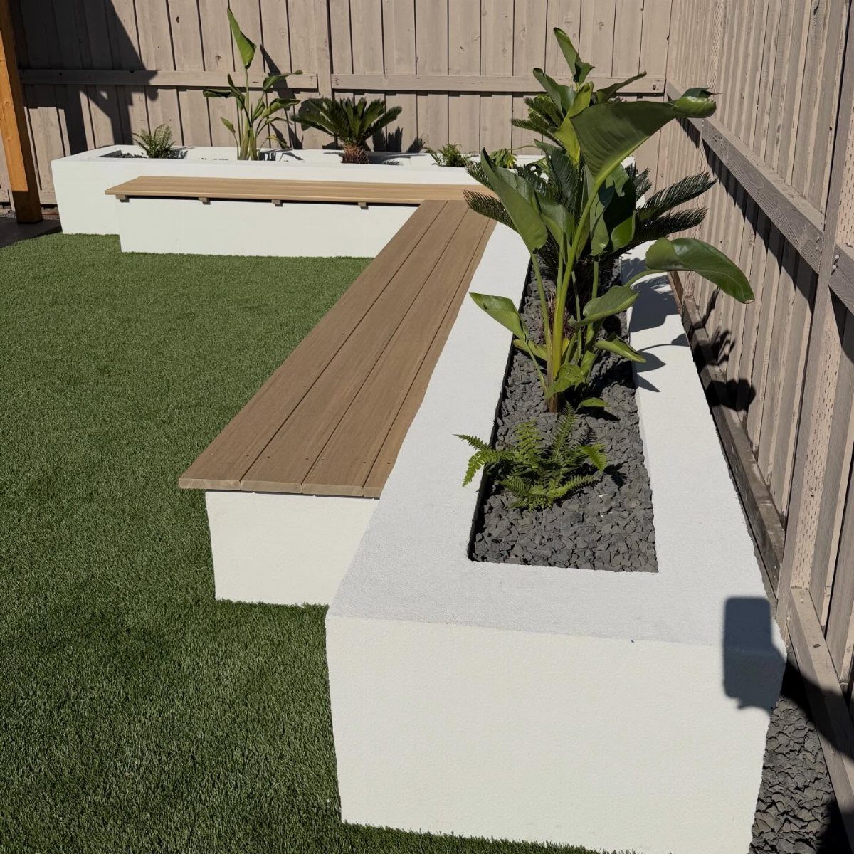 White concrete low planters with wooden benches and tropical plants on green turf.