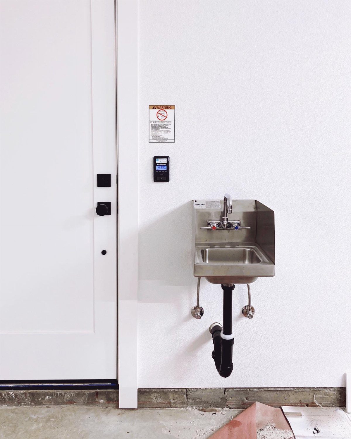 Stainless steel utility sink mounted on a white wall with exposed plumbing underneath.