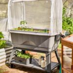 A grey portable raised planter box with a mesh cover on wheels in a garden.