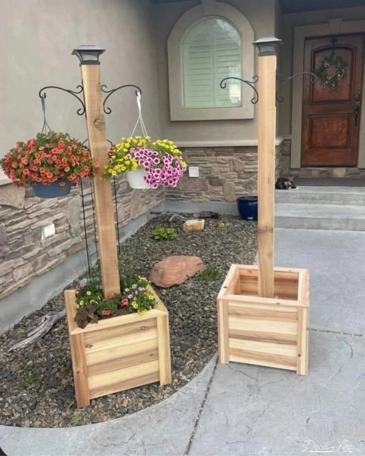 Two tall wooden planter boxes with vertical posts and hanging flower baskets in a garden.