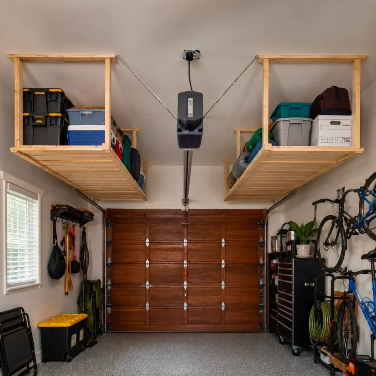 Wooden overhead storage shelves mounted to a garage ceiling holding various plastic storage bins.